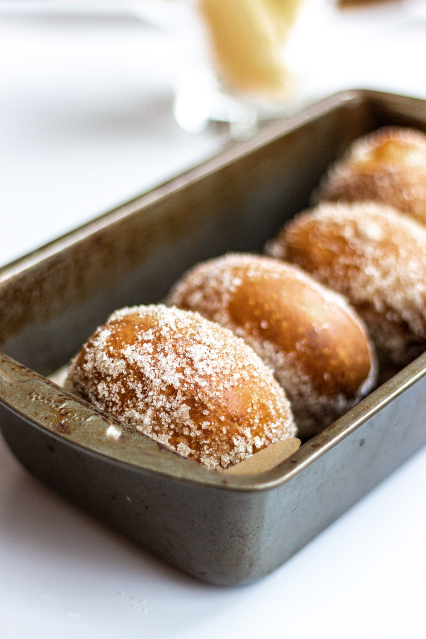 4 donuts coated in cardamom sugar sitting in a grey loaf pan.